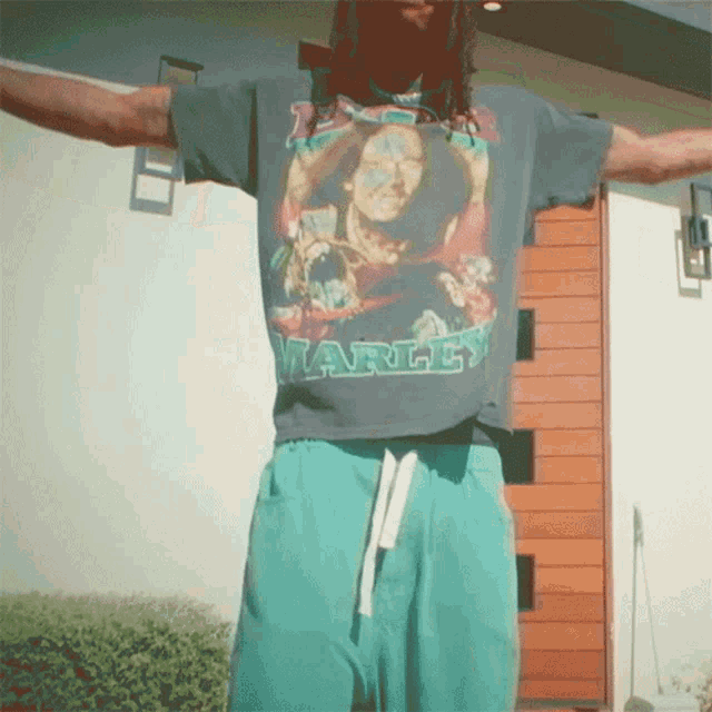 a man wearing a shirt that says marley is standing in front of a house