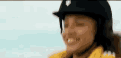 a woman wearing a helmet and a yellow jacket is smiling and looking at the camera .