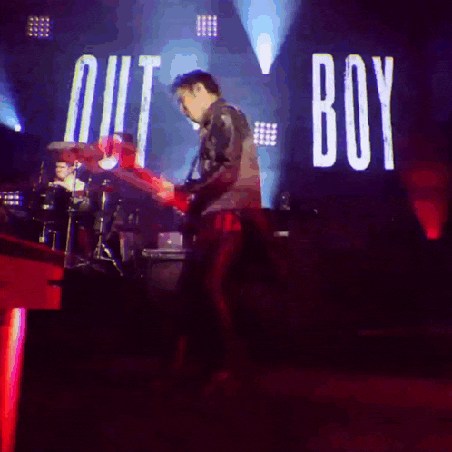 a man playing a guitar in front of a sign that says " out boy "