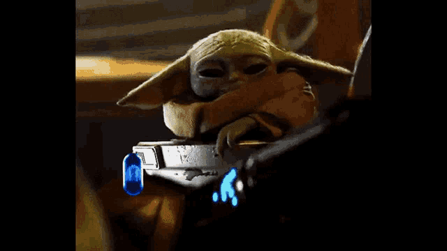 a baby yoda is sitting in a crib in a dark room with a blue light behind it .