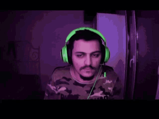 a man wearing green headphones and a camouflage shirt is smiling .