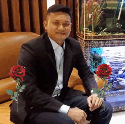 a man in a suit sits in front of a fish tank with red roses in front of him