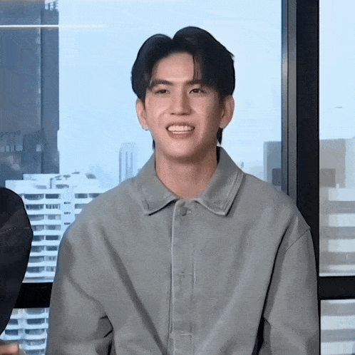 a young man wearing a grey shirt is smiling in front of a window