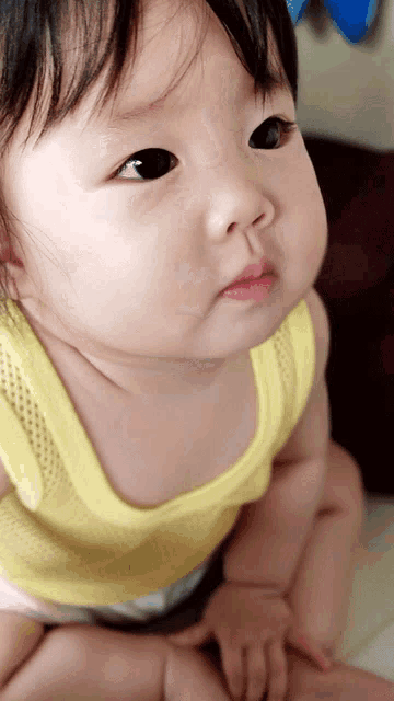 a baby in a yellow tank top is looking up