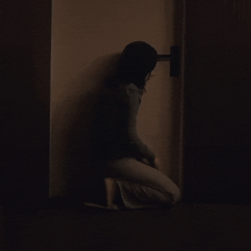 a woman is kneeling down in a dark room looking at a door