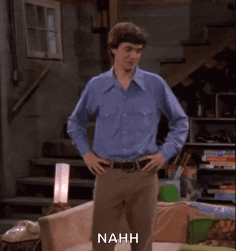 a man in a blue shirt is dancing in a living room with the word nahh above him