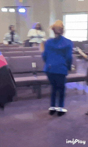 a woman in a blue jacket is dancing in a church with the words imgplay visible on the bottom