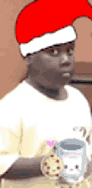 a man wearing a santa hat is holding a cup and cookie .