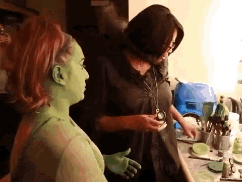 a woman with green face paint talks to another woman