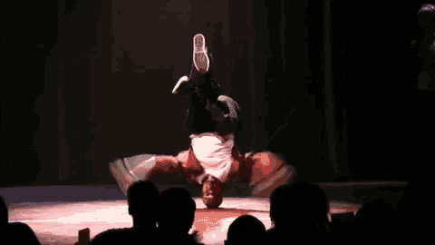 a man doing a handstand on a stage with a crowd watching