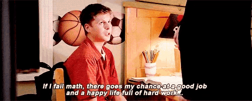 a boy in a red shirt is sitting at a desk with a basketball on the wall .
