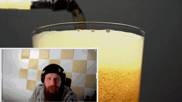 a man with a beard wearing headphones is looking at a glass of beer
