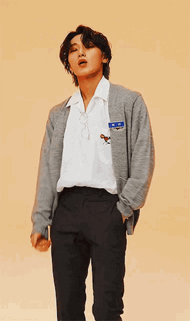 a young man wearing a gray cardigan and a white shirt with a name tag on his chest