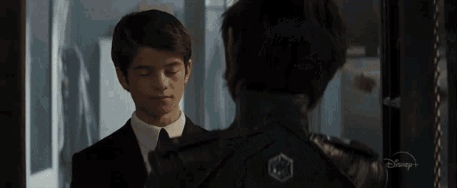 a man in a suit and tie is standing next to another man in a suit and tie with a disney + logo on his back