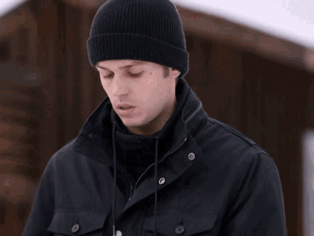 a man wearing a black jacket and a black beanie looks at the camera
