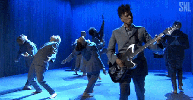 a man playing a guitar in front of a group of dancers with snl written on the bottom
