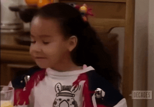 a little girl is sitting at a table with a glass of orange juice and a zebra shirt on .
