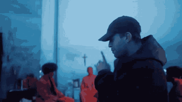 a man wearing a black hat stands in front of a cross