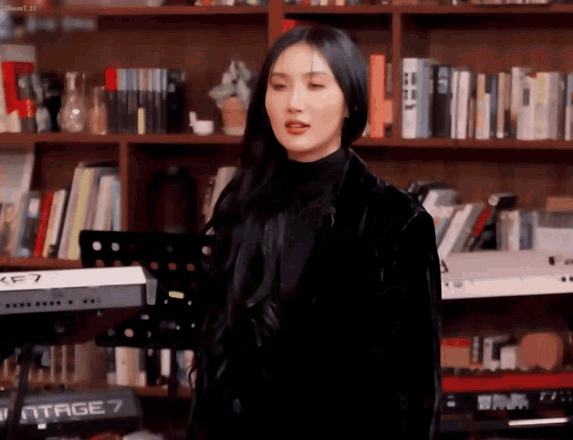 a woman in a black jacket is standing in front of a piano in a library .