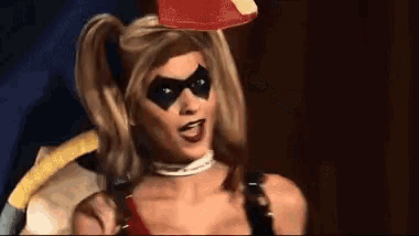 a woman in a harley quinn costume is standing in front of a black curtain .