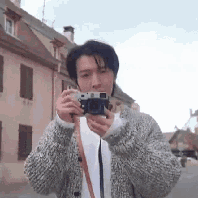 a man in a sweater is taking a picture of a building with a camera .