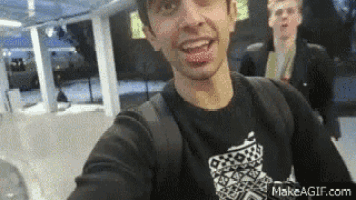 a man in a black shirt is taking a selfie with another man behind him .