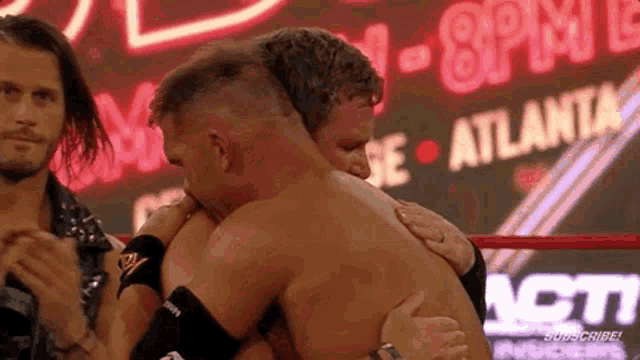 two men are hugging each other in a wrestling ring in front of a neon sign .