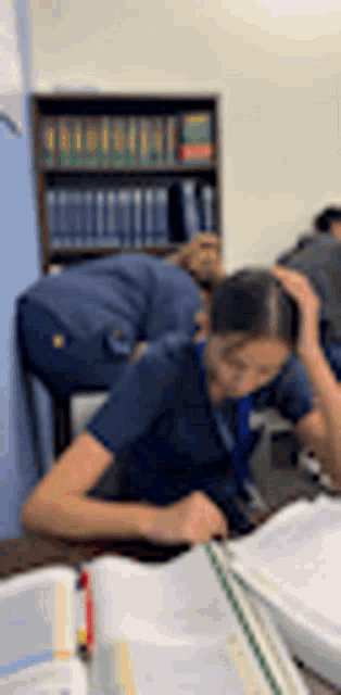 a woman is sitting at a desk with her hands on her head and a bookshelf in the background .