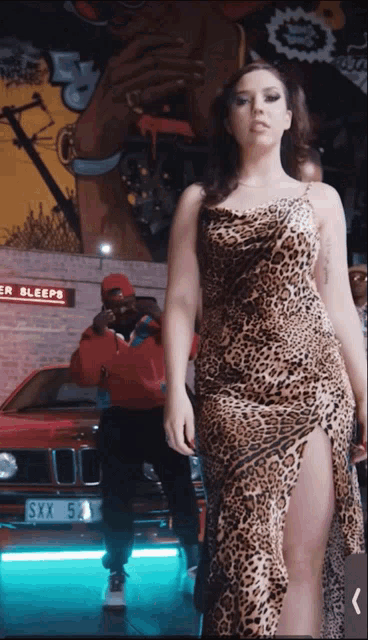 a woman in a leopard print dress is standing in front of a red car