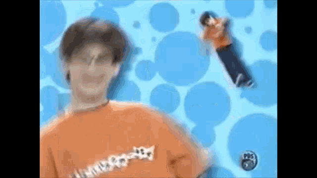 a man in a orange shirt is standing in front of a blue background .