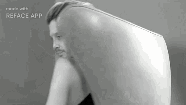 a black and white photo of a man with a beard sitting in front of a large white object .