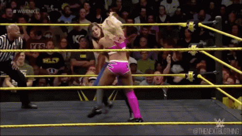 two women are wrestling in a ring with a referee and a crowd watching .