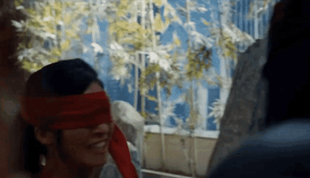 a woman wearing a red blindfold is smiling in front of a window
