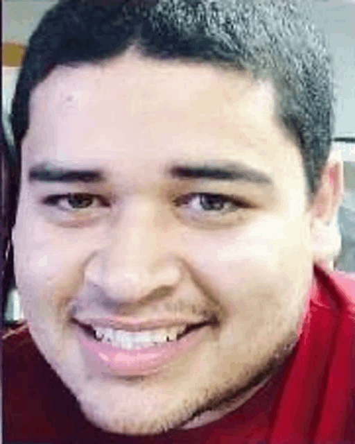 a close up of a man 's face with a beard wearing a red shirt and smiling .