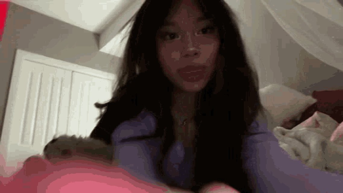 a girl with long hair is laying on a bed with her tongue out