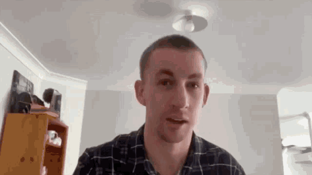 a man in a plaid shirt is looking at the camera in a living room .