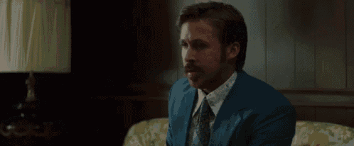 a man in a blue suit and tie is sitting on a couch with his hands folded .
