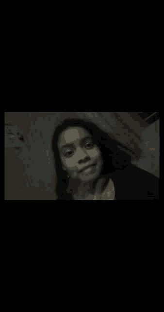a woman is taking a selfie in a dark room with a black background .