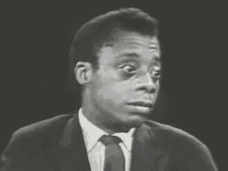 a man in a suit and tie is smoking a cigarette and looking at the camera .