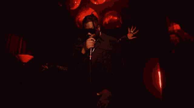 a man in a black suit is singing into a microphone in a dark room