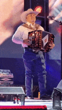 a man in a cowboy hat is playing an accordion on stage