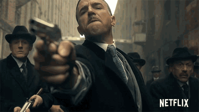 a man in a suit and tie is pointing a gun with a netflix logo in the background
