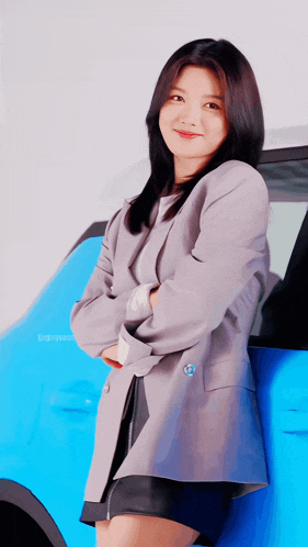 a woman in a grey jacket is leaning on a blue car