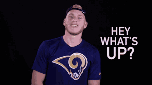 a man wearing a blue shirt with a ram on it is smiling and says hey what 's up