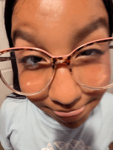 a girl wearing glasses and a blue shirt with butterflies on it makes a funny face