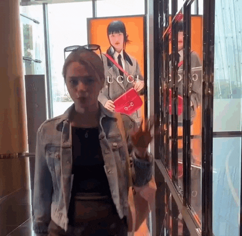 a woman in a denim jacket is standing in front of a gucci sign