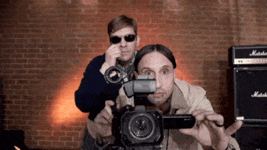 a man is holding a sony camera while another man looks on