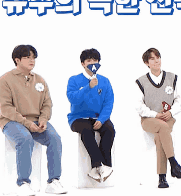 a man in a blue sweater with the letter a on it sits next to two other men