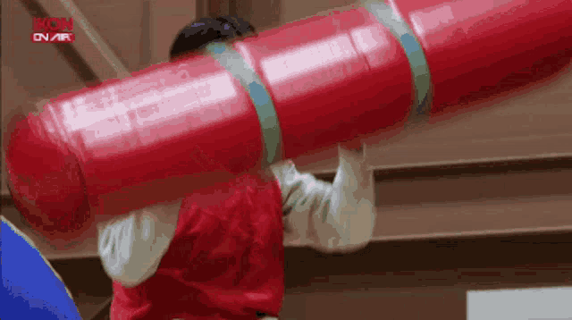 a person in a red vest is holding a large red object in front of a sign that says rkom on air