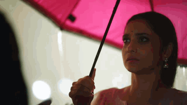a woman is holding a pink umbrella and looking at the camera